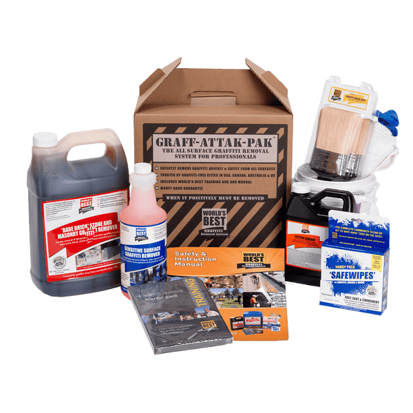 A comprehensive Graff-Attak-Pak graffiti removal system kit displayed on a clean white background. The kit includes a large jug of dark liquid, a pink bottle of cleaning solution, a cardboard box of safety gloves, a brush, a can of compressed air, a box of safety wipes, and an instruction manual.