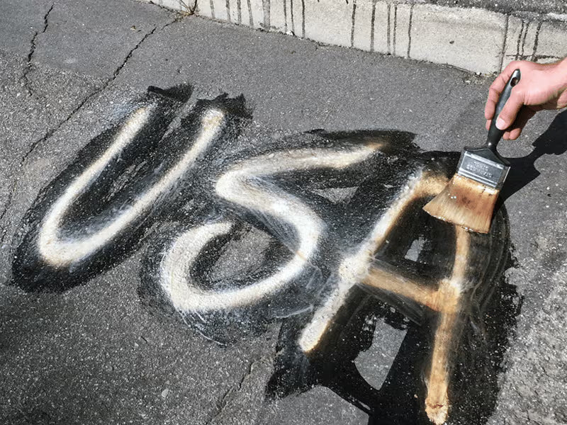 Removing white spray painted graffiti from asphalt.