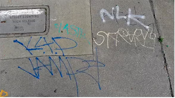 
Blue and white spray-painted graffiti on a concrete sidewalk.