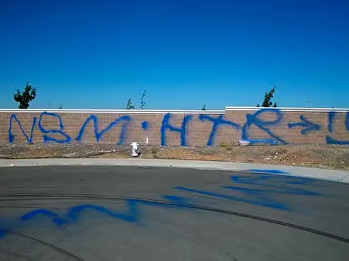 Blue spray-painted graffiti on a block wall and asphalt.