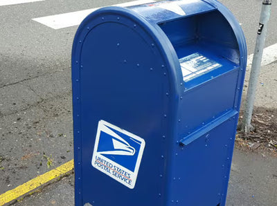 A blue United States Postal Service mailbox on an outdoor street corner, with the USPS logo visible on the front.